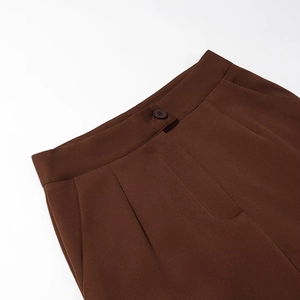Close-up of high-waisted brown suit pants featuring resin button and pleat details
