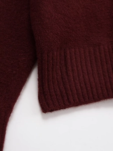 Détail macro d'un pull en maille bordeaux montrant la texture douce et les bords-côtes