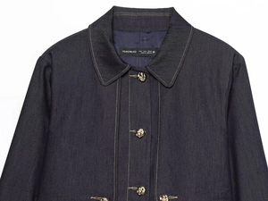 Detail of dark blue denim jacket with contrast white stitching and gold knot buttons