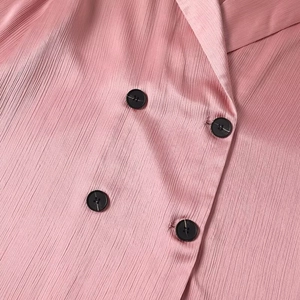 Close-up of pink pleated fabric with black buttons and classic notched lapel blazer detail