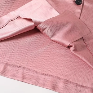 Detail of pink pleated fabric texture with a black button and fine hem stitching on a suit