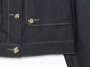 Detail of dark indigo denim jacket with gold knot buttons and contrast topstitching