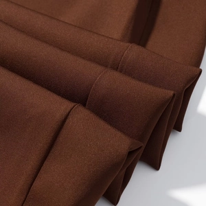 Detail shot of the dark brown fabric texture and draped layers of women's suit pants
