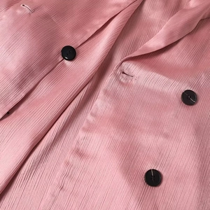 Macro shot of pink pleated satin fabric with elegant black buttons on the blazer front
