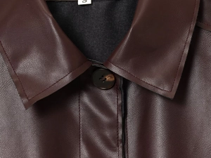 Détail du col à revers et du bouton marbré sur la veste en simili cuir bordeaux