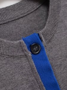 Detail of round neck gray knit cardigan with royal blue trim and black button