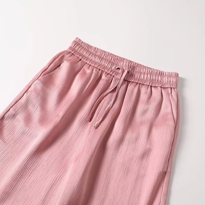 Detail of pink satin pleated trousers featuring elastic waist with adjustable drawstring
