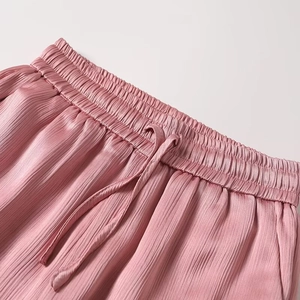 Close-up of pink pleated satin trousers featuring elastic waistband and drawstring detail