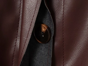 Détail de veste en cuir PU brun rouge foncé avec texture litchi et bouton écaille de tortue