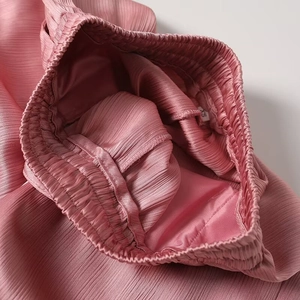Detail of pink pleated fabric with elastic waist and size label on female trousers