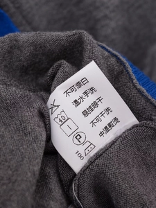 Detailed view of white satin care label on dark grey knit cardigan with blue trim