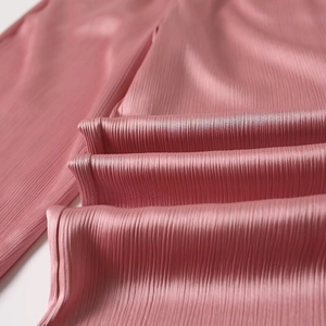 Close-up of pink satin pleated wide-leg trousers with vertical pleats and glossy finish