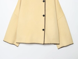 Detail of cream wool jacket featuring black blanket stitch trim and round buttons