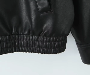 Detail of the elastic hem and precise stitching on the black PU leather jacket