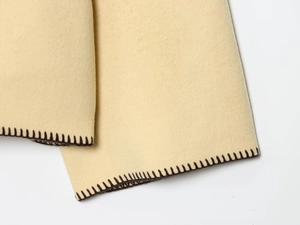 Close-up of beige faux wool fabric with brown overlock stitching detail on the jacket