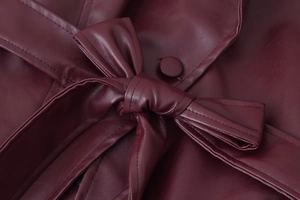 Détail du nœud à la taille et des coutures sur la veste en similicuir bordeaux