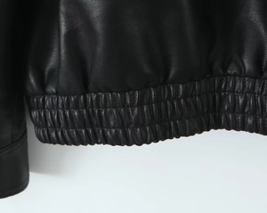 Detail of the black PU leather jacket showing the elasticized hem and litchi grain texture