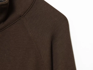 Detail shot of a dark brown zip-up sweater showing high-density knit fabric and raglan sleeves