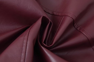 Vue macro du cuir PU bordeaux avec texture litchi et détails de couture fine à double ligne