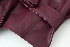 Détail de la veste en similicuir bordeaux montrant la taille ceinturée et les coutures