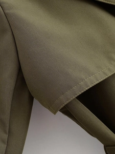 Detail view of olive green trench coat featuring precision double-row stitching on fabric