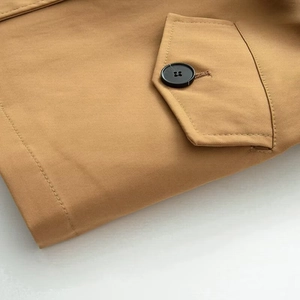 Détail d'un trench camel avec bouton noir, poche à rabat et texture de tissu en sergé