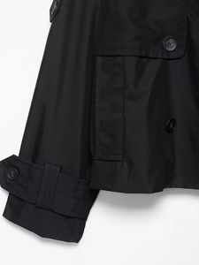Détail de la manche d'un trench-coat noir avec bouton et texture de tissu sergé