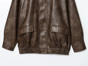 Close-up of vintage brown PU leather jacket featuring flap pockets and elastic hem details
