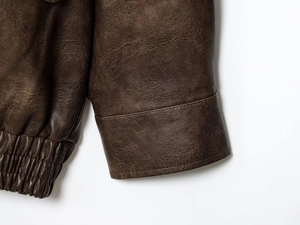 Detailed close-up of brown PU leather jacket featuring elasticized hem and textured cuffs