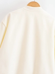 Macro detail of the cream-colored bomber jacket with ribbed collar and soft fabric texture