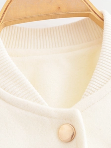 Close-up of beige bomber jacket featuring ribbed collar and polished gold metal button