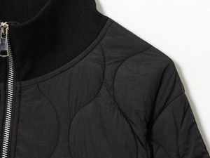 Detail of black quilted jacket featuring metal zipper and ribbed stand collar design