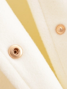 Detailed macro view of premium rose gold metal snap buttons on cream wool blend fabric