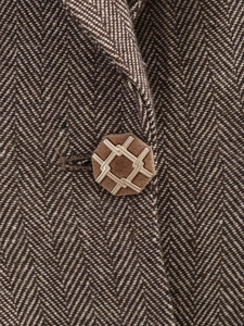 Macro detail of brown herringbone wool fabric and vintage gold braided hexagonal button