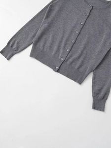 Detailed view of gray knit cardigan featuring round neck and ribbed cuffs on white background