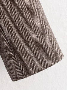 Close-up of brown and white herringbone wool fabric texture on a woman blazer sleeve