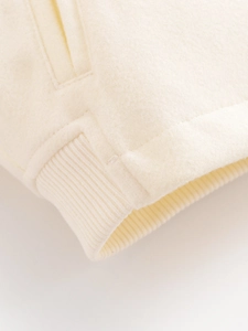 Detail of cream jacket featuring soft wool texture and premium ribbed cuff stitching