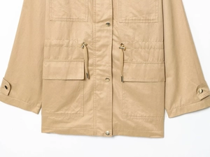 Detail of khaki utility jacket showing drawstring waist, flap pockets, and metal buttons