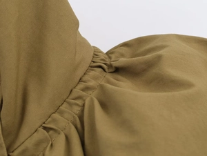 Detailed macro view of the olive green gathered hem and pleated fabric of the bomber jacket