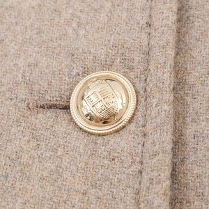 Macro shot of an antique gold coat button with crest detail on beige wool fabric