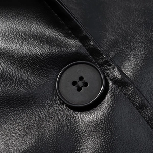 Close-up of matte black button and textured faux leather grain on long trench coat