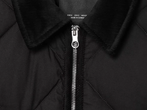 Détail d'une veste matelassée noire avec col en velours côtelé et zip métallique