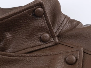 Dettaglio macro della giacca in pelle PU marrone scuro con trama litchi e bottoni