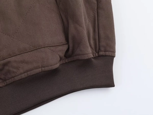 Detail of quilted brown bomber jacket featuring diamond stitching and ribbed hem