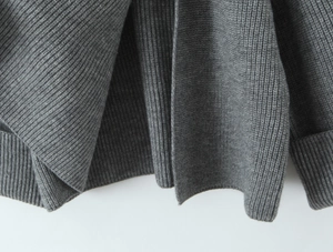 Close-up of grey knit sweater showing thick ribbed texture and wide folded cuffs