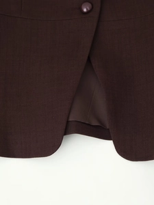 Close-up of the curved hem and button on a dark brown street style suit vest