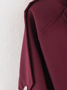 Détail du trench-coat bordeaux avec coutures renforcées et sangle à bouton