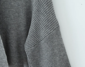 Detail of grey chunky knit ribbing texture on the shoulder and sleeve of a loose sweater