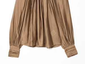 Detailed view of the pleated cuffs and smooth satin texture on this bronze long sleeve top