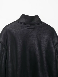 Détail du col montant et de l'empiècement en cuir sur une veste en daim noir de qualité